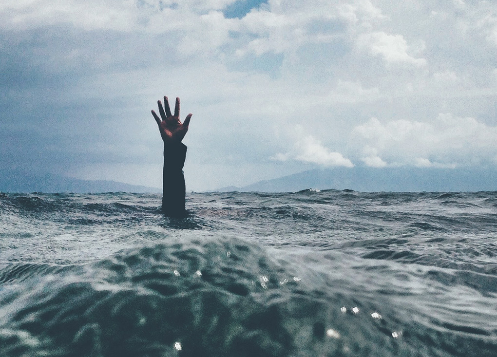 Eine Hand ragt hilfesuchend aus den Wellen im Ozean hervor. Versunken im Alltag.