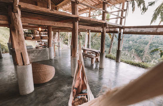Retreat-Urlaub: Eine Person entspannt in einer Hängematte, die in einem offenen Holzhaus mit Blick auf den Dschungel hängt.