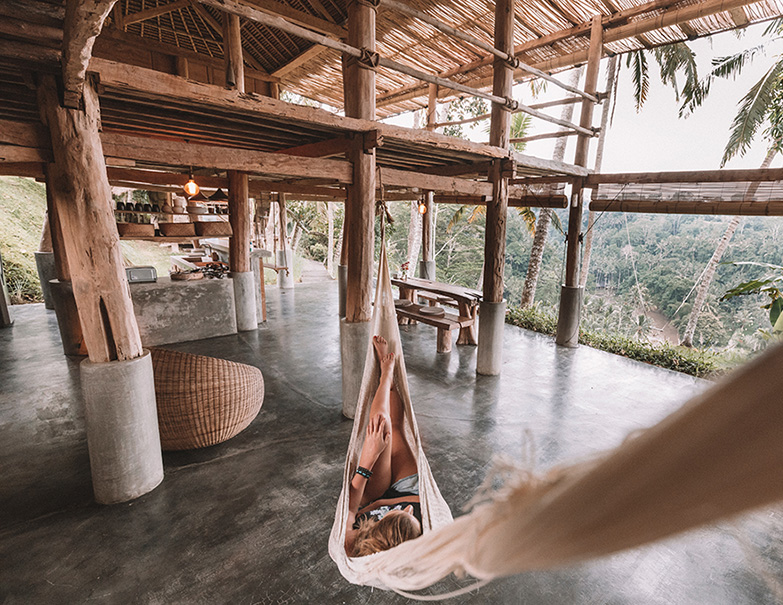 Retreat-Urlaub: Eine Person entspannt in einer Hängematte, die in einem offenen Holzhaus mit Blick auf den Dschungel hängt.