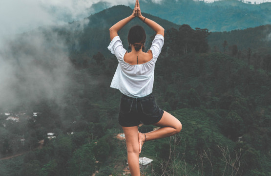 Yoga für Anfänger: Eine Frau macht eine Yoga Pose in den Bergen, umringt von Bäumen und mystischem Nebel.