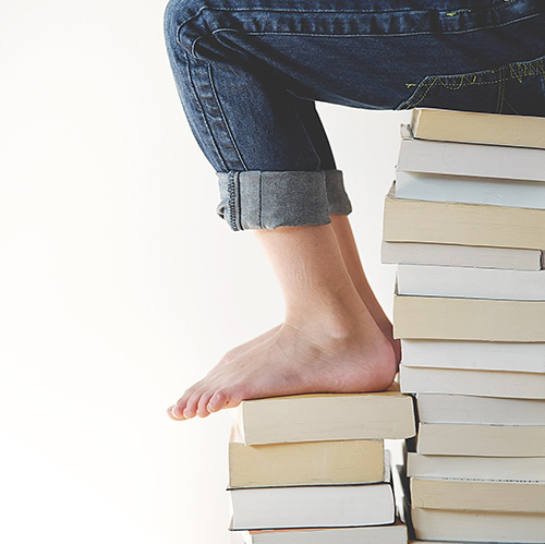 TheCalmBase | Bildung – Eine Frau sitzt auf auf einem Bücherstapel