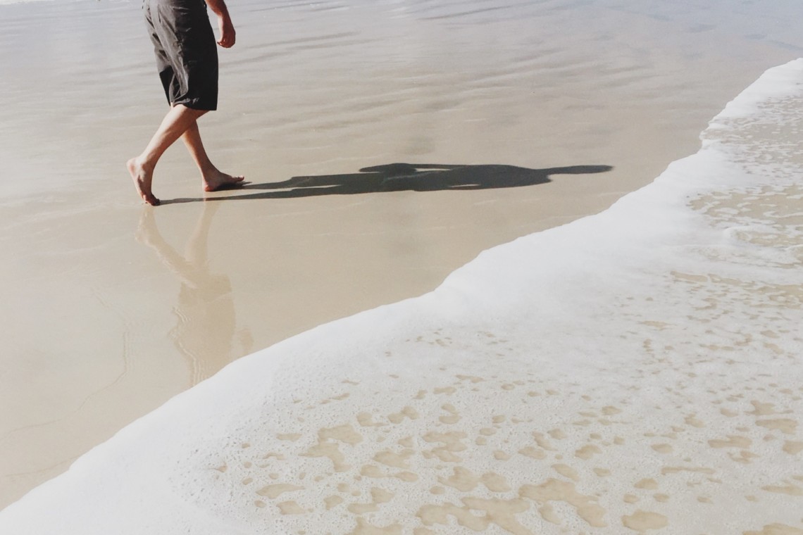 Achtsamkeit während der Corona-Krise: ein Mann spaziert am Strand entlang und genießt den Sand zwischen seinen Zehen.