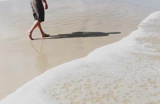 Achtsamkeit während der Corona-Krise: ein Mann spaziert am Strand entlang und genießt den Sand zwischen seinen Zehen.