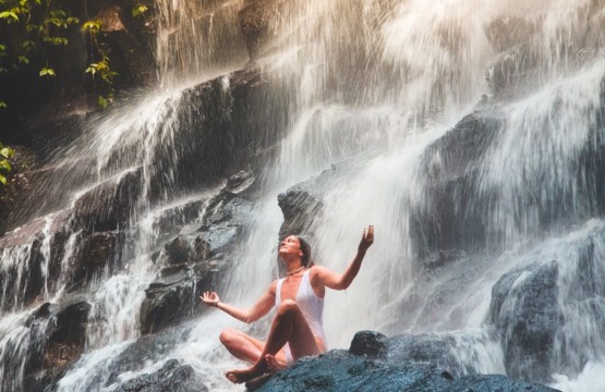 TheCalmBase | Frau meditiert unter einem Wasserfall