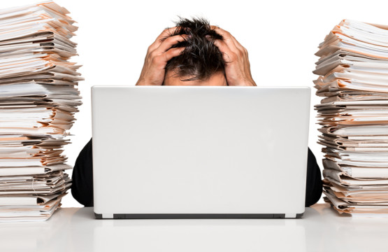 Stress im Büro. Ein Mann versinkt zwischen Aktenstapeln und Computer