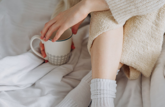 Eine Frau trinkt einen Kaffee im Bett – so kann auch eine gesunde Morgenroutine aussehen.